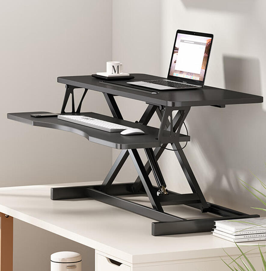 Black height adjustable standing desk converter on a white office desk, featuring a two-tier design with a laptop and monitor on the top tier, and a keyboard and mouse on the lower tier.